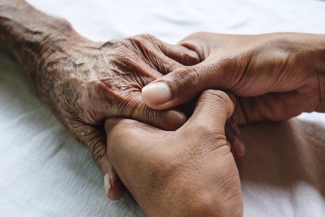 Hands of the old man and a man hand on the white bed